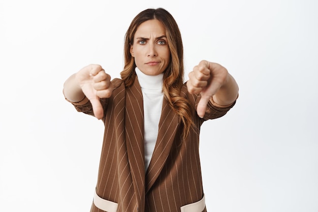 Disappointed saleswoman showing thumbs down Businesswoman dislike product expresses negative opinion bad quality white background