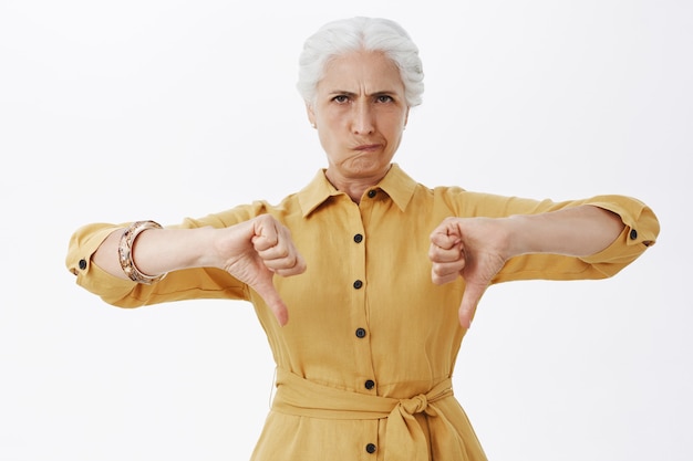 Free photo disappointed senior lady frowning and showing thumbs-down