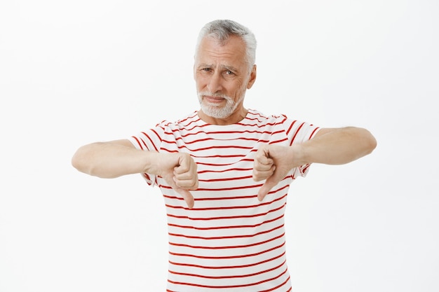 親指を下に向けてTシャツを着た失望した年配の男性、嫌いなジェスチャーを示す