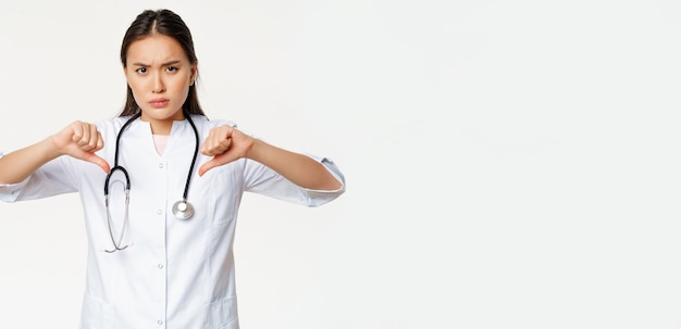 Foto gratuita il medico dell'ospedale femminile asiatico serio deluso mostra i pollici giù con disapprovazione