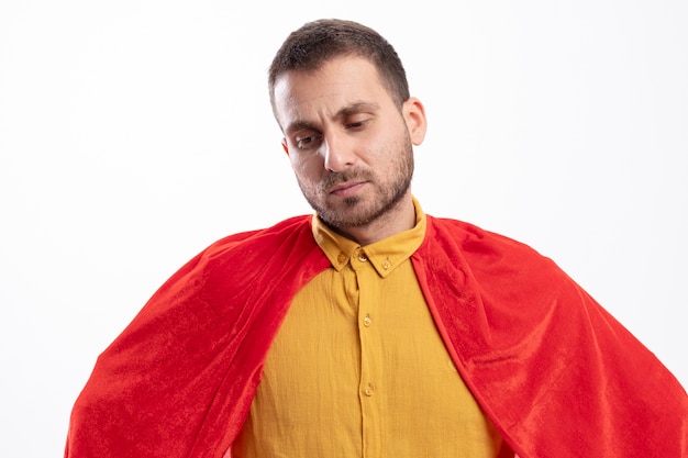 Free photo disappointed superhero man with red cloak looks down isolated on white wall