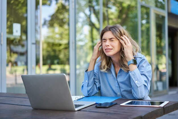 Disappointed young businesswoman feeling frustrated sitting with laptop outdoors on street looking u