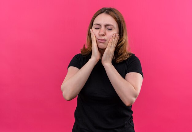 Разочарованная молодая случайная женщина кладет руки на щеки с закрытыми глазами на изолированное розовое пространство с копией пространства