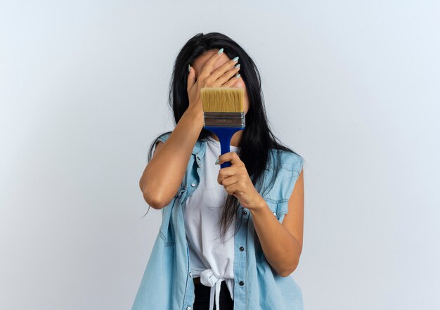 Disappointed young caucasian girl puts hand on face and holds painting brush 