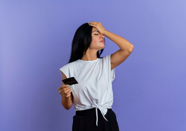 Disappointed young caucasian woman puts hand on forehead and holds credit card