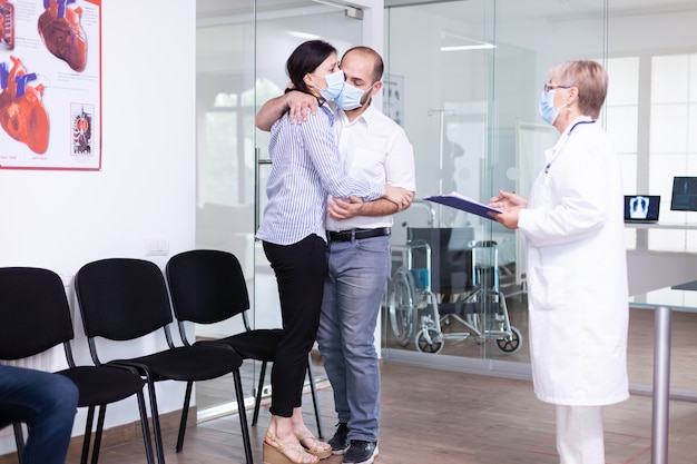 Disappointed young couple in hospital waiting area from doctor unfavorable bad news during coronavirus outbreak