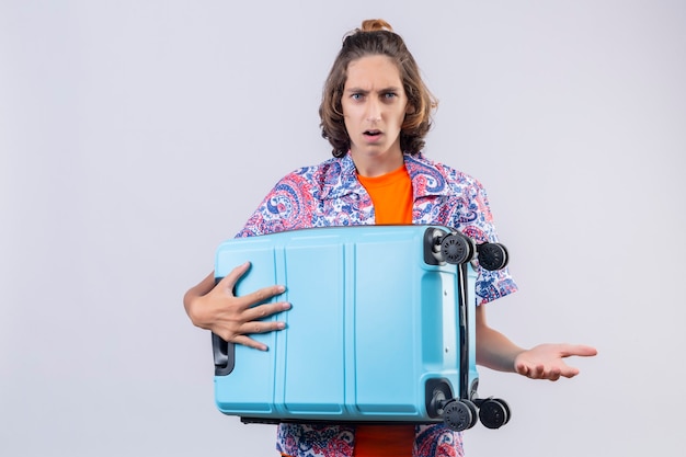 Disappointed young handsome guy holding travel suitcase looking surprised standing 