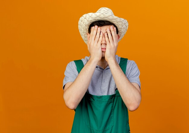 Disappointed young male gardener wearing gardening hat puts hands on face