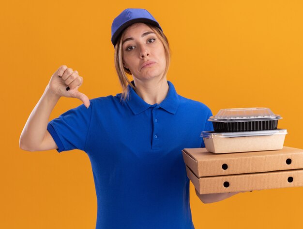 Giovane ragazza graziosa di consegna delusa in uniforme pollici giù e tiene i pacchetti di cibo di carta