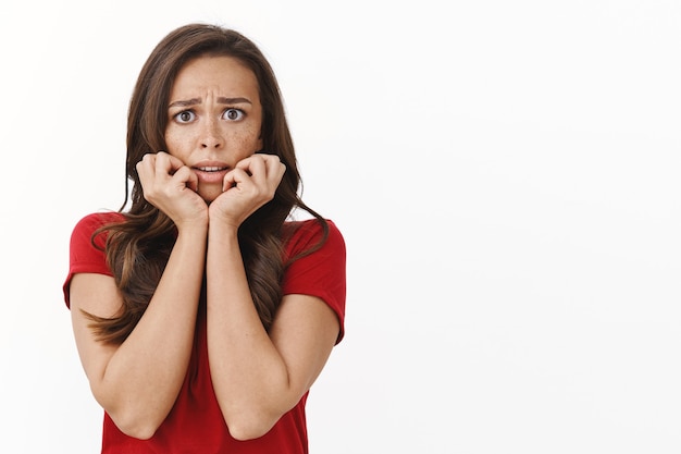 Free photo disappointed young upset and hurt timid brunette woman feeling scared, afraid of strange noise in dark, hold hands near mouth, frowning trembling fear, staring frightened