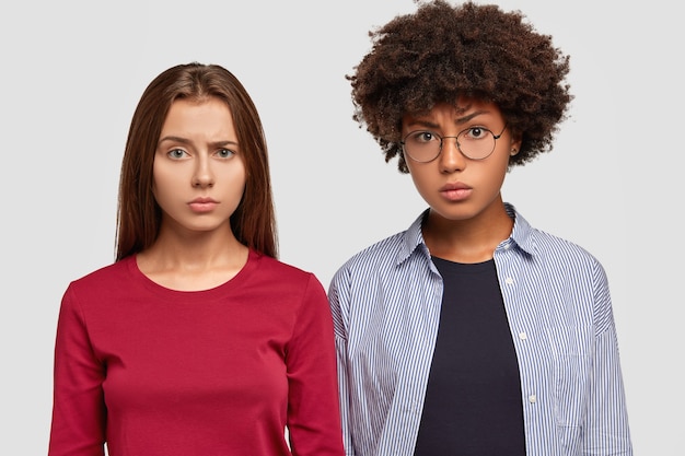 Free photo discontent mixed race women frown faces in displeasure, stand closely to each other