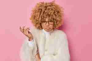 Free photo discontent unhappy curly haired woman shrugs shoulder feels indignant faces difficult choice has sad expression wears eyeglasses white coat isolated over pink background. so what should i do