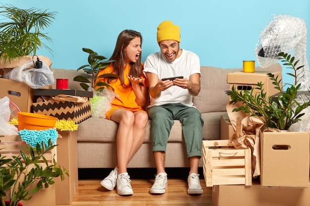 Free photo discontent young couple sitting on the couch surrounded by boxes