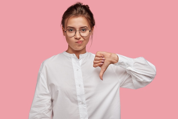 Discontent young woman with glasses posing against the pink wall