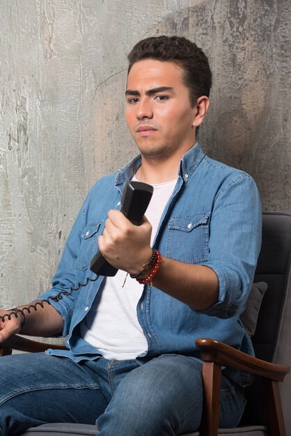 Disgruntled man holding handset and sitting on chair. High quality photo