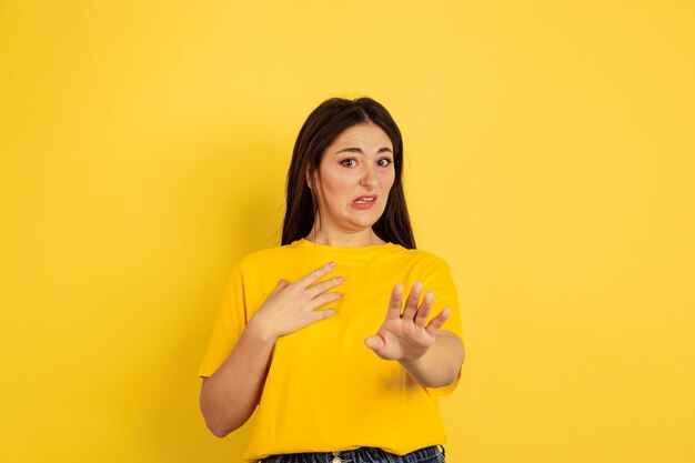 Disguasted. Caucasian woman's portrait isolated on yellow studio background. Beautiful female brunette model in casual style. Concept of human emotions, facial expression, sales, ad, copyspace.