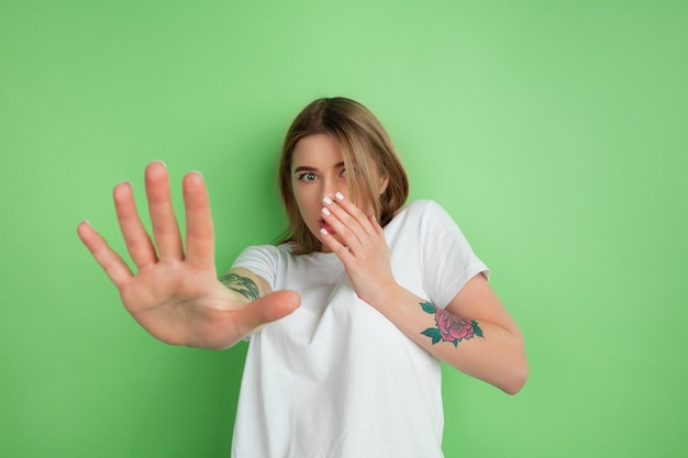 Disguasted. Caucasian young woman's portrait isolated on green studio wall