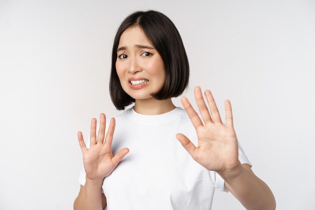 Disgusted asian woman rejecting smth grimacing from dislike and aversion stare with cringe refusing offer standing over white background