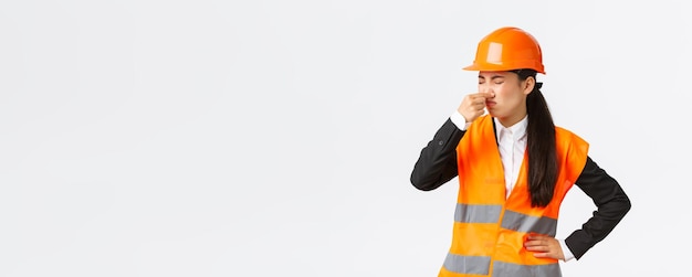 Free photo disgusted and displeased asian female architect enter construction area and shut ears as smell disgusting reek awful smell grimacing from discomfort standing in safety helmet over white background