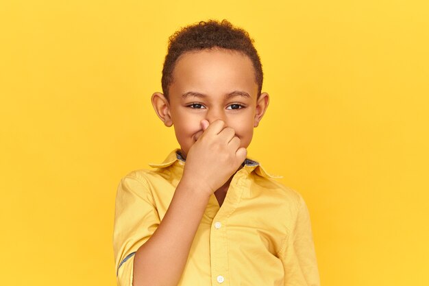 Disgusted displeased dark skinned boy pinching nose with fingers, holding breathe because of unpleasant gross stink from sweaty armpits or dirty socks