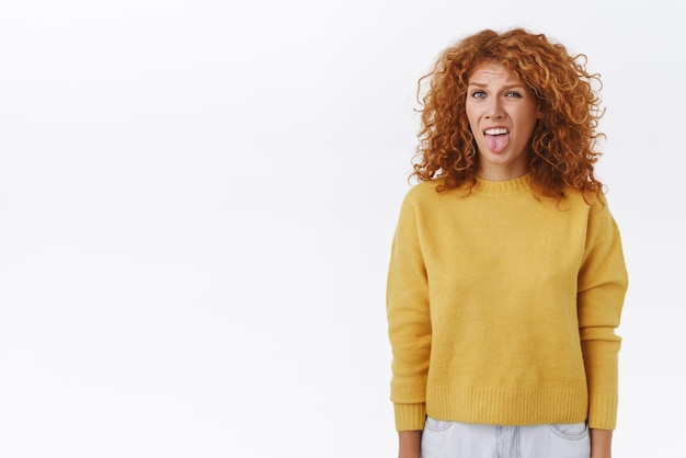 Disgusted displeased silly redhead ginger girl stick tongue and grimacing cringe from awful smell want puke from bad reek standing displeased unsatisfied over white background express aversion