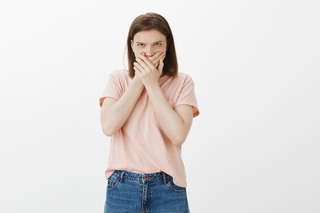 Disgusted and mad woman shut mouth with hands, looking with hatred