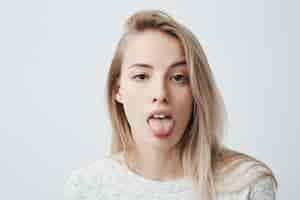 Free photo disgusted pretty young woman with blonde hair sticking out tongue expressing her dislike or disregard towards something funny humorous female model showing tongue at camera as if teasing someone