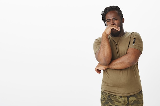 Disgusted unhappy guy in a brown t-shirt posing against the white wall