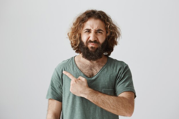 Disgusted and upset grimacing middle-eastern man pointing finger left at bad thing