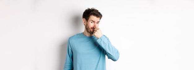 Disgusted young man in sweatshirt shut his nose looking at something with bad smell standing over wh