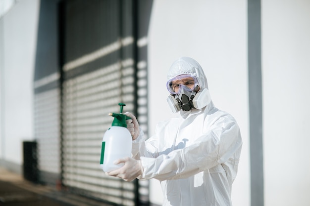 Disinfection specialist staff in personal protective equipment (ppe) suit, gloves, mask and face shield, cleaning Quarantine area with a bottle of pressurized spray disinfectant to remove covid-19