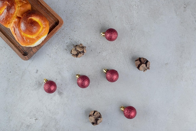 Free photo display of christmas balls and a sweet bun on marble table.