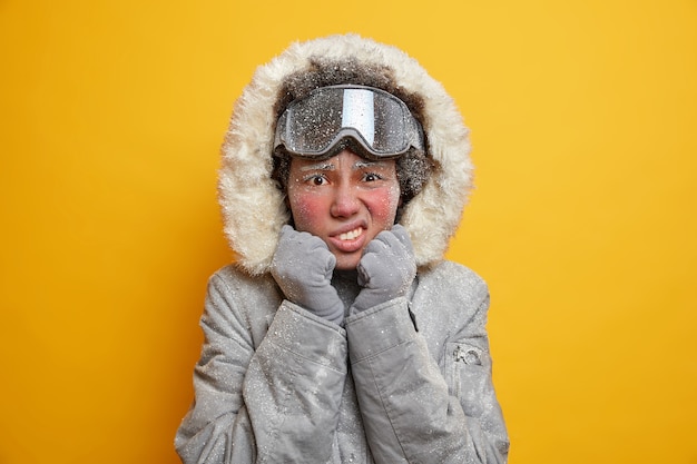 Недовольная афроамериканка с лицом, покрытым льдом, стискивает зубы от холодного взгляда, несчастно носит куртку и лыжные очки, наслаждается летними каникулами, дрожит в морозную погоду.