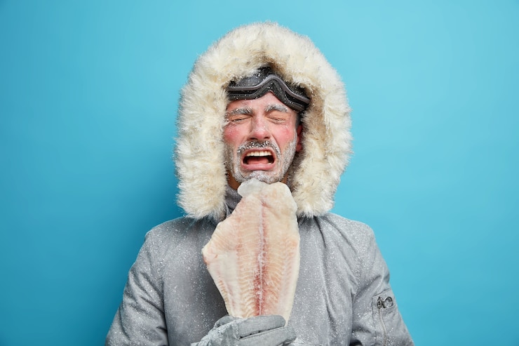 Free Photo displeased arctic person covered with frost during severe cold day freezing climate and weather holds frozen fish lives in northern parts. male eskimos in outerwear.