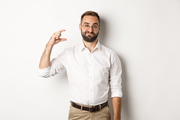 Displeased bearded businessman showing small gesture, looking disappointed, standing against white