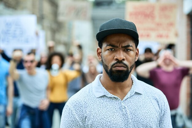 Displeased black man looking at camera while being on public antiracism demonstrations Crow of people is in the background