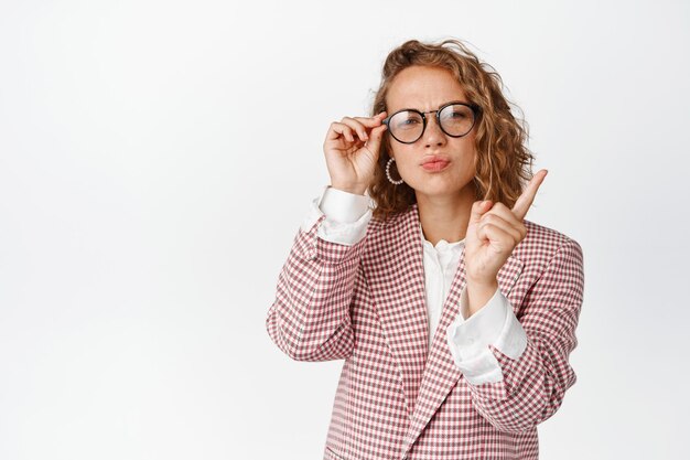 Displeased blond woman shaking finger, looking at camera in glasses, scolding bad behaviour, standing disappointed against white background