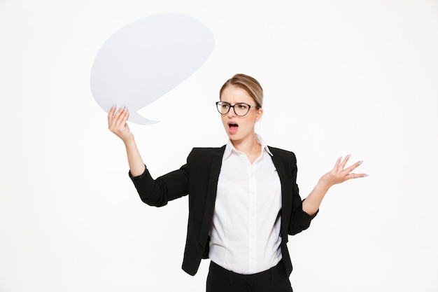 Free photo displeased blonde businesswoman in eyeglasses looking aside and holding blank speech bubble over white ackground