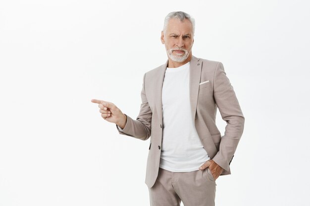 Displeased bothered businessman in suit pointing finger left and grimacing disappointed