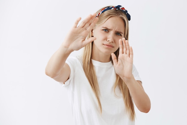 Displeased and bothered young blond girl posing against the white wall