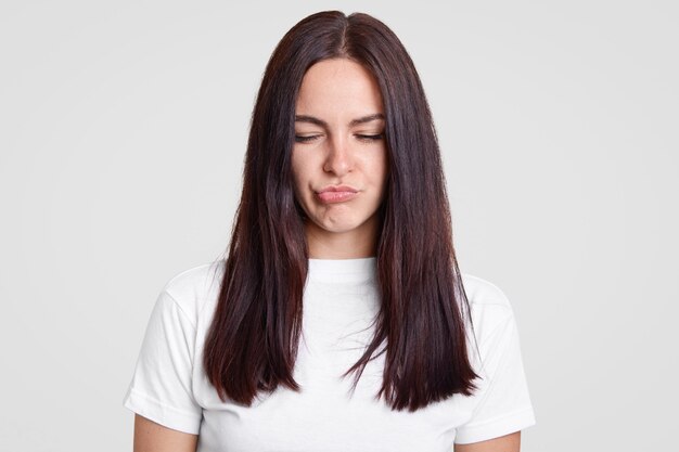 Displeased brunette young girl pouts lips, has discontent facial expression, hears negative comments about her work