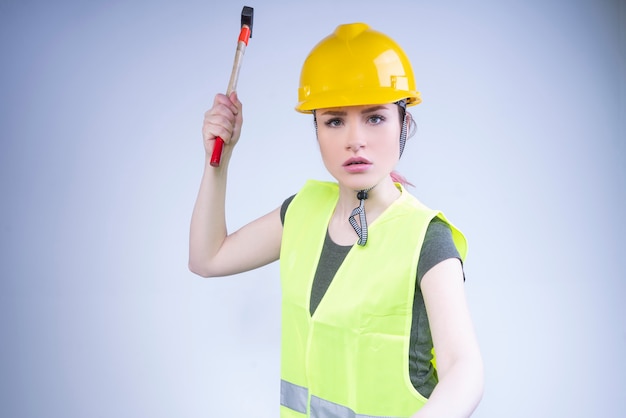 Displeased builder in a yellow work vest swinging a hammer