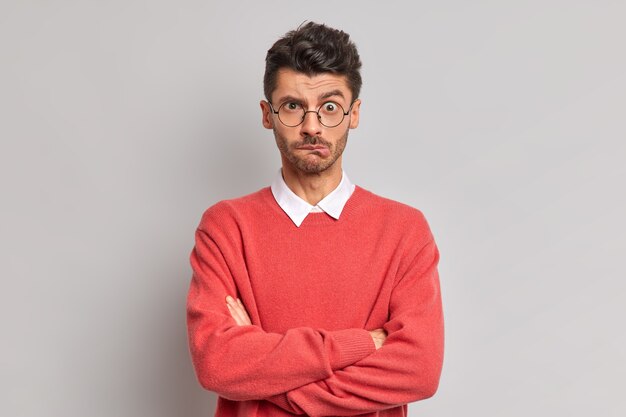 Displeased Caucasian man bites lips keeps hands crossed dissatisfied with something