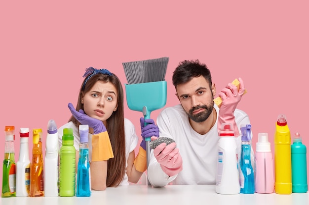 Displeased Caucasian woman and man look with displeasure, feels fatigue after spring cleaning in house, use broom