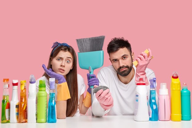 不機嫌な白人の女性と男性は不快に見え、家の大掃除の後に疲労感を感じ、ほうきを使用します