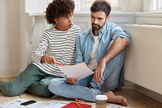 Displeased dark skinned businesswoman convinces her husband to pay attention at some figures in financial report