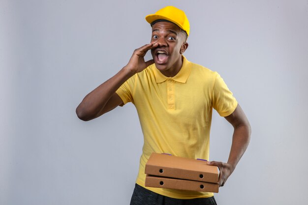 노란색 폴로 셔츠와 모자 입 서 근처 손으로 외치는 피자 상자를 들고 불쾌 배달 아프리카 계 미국인 남자