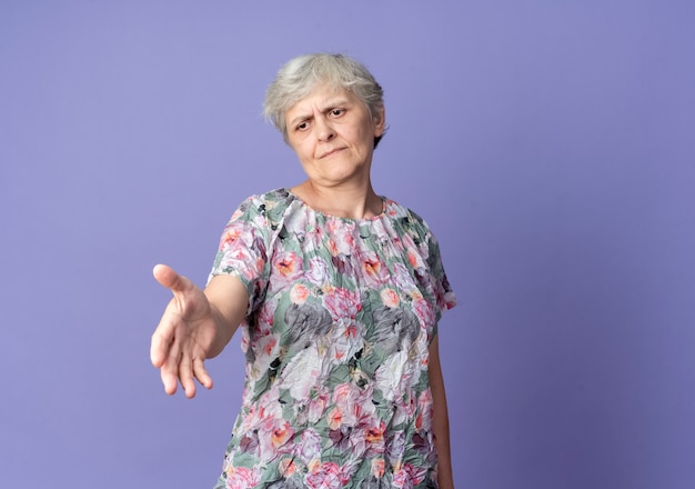 Displeased elderly woman holds hand out isolated on purple wall