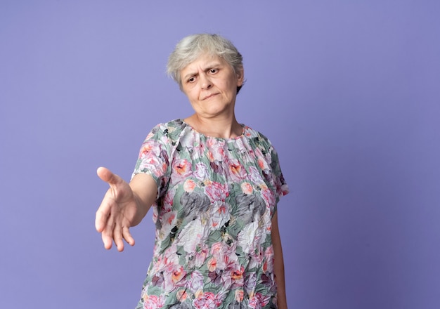 不機嫌な年配の女性は紫色の壁に隔離された手を差し伸べる
