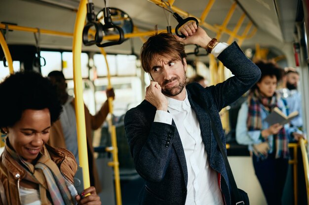 Недовольный предприниматель звонит по телефону, пока едет на работу на автобусе
